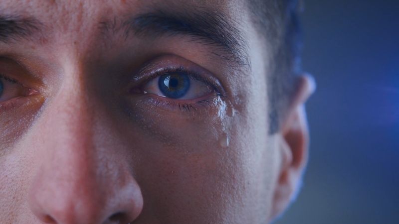 A close-up of a man’s face with a single tear running down his cheek