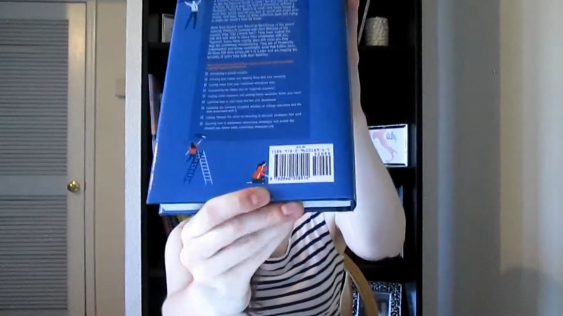 A person holds up a blue book showing the barcode on the back cover