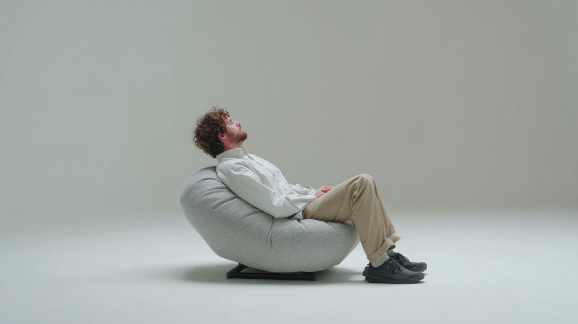 Person sitting back relaxed on a modern cushioned chair in a minimalist setting, appearing calm and reflective