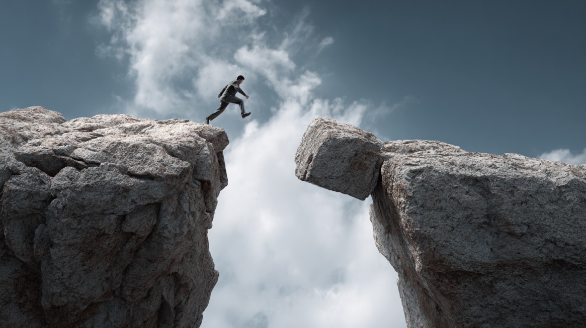 Person jumping across a wide gap between two rocky cliffs under a cloudy sky, symbolizing courage and determination
