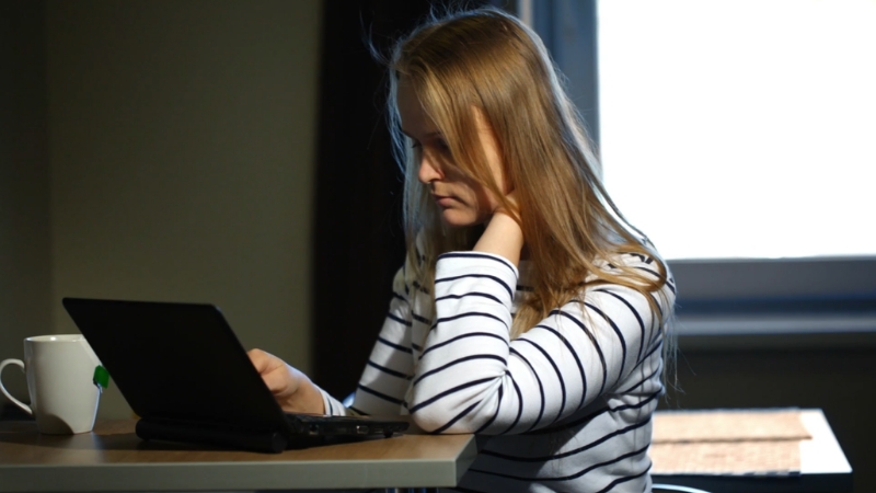A woman sits at a table focused on her laptop with a cup beside her
