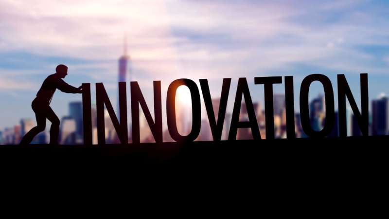 A person pushes large letters that spell “Innovation” against a blurred city skyline in the background