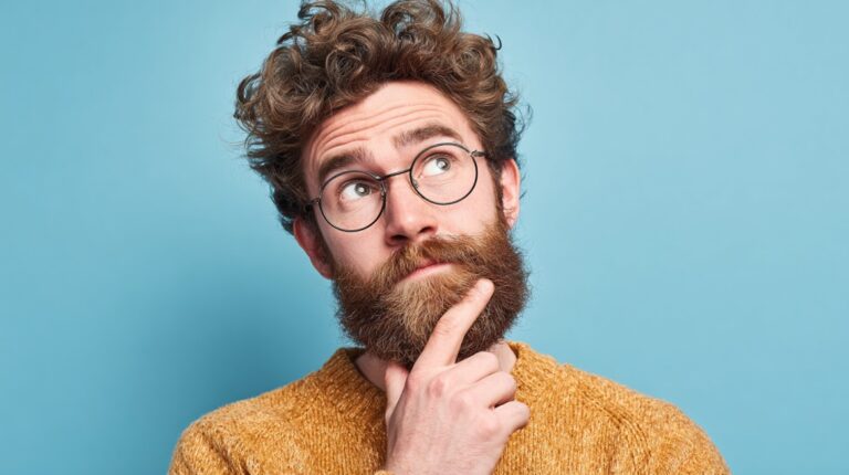 Bearded man with glasses looking up thoughtfully against a blue background