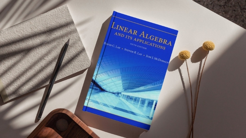 David Lay Linear Algebra textbook on a desk next to a notebook and pen