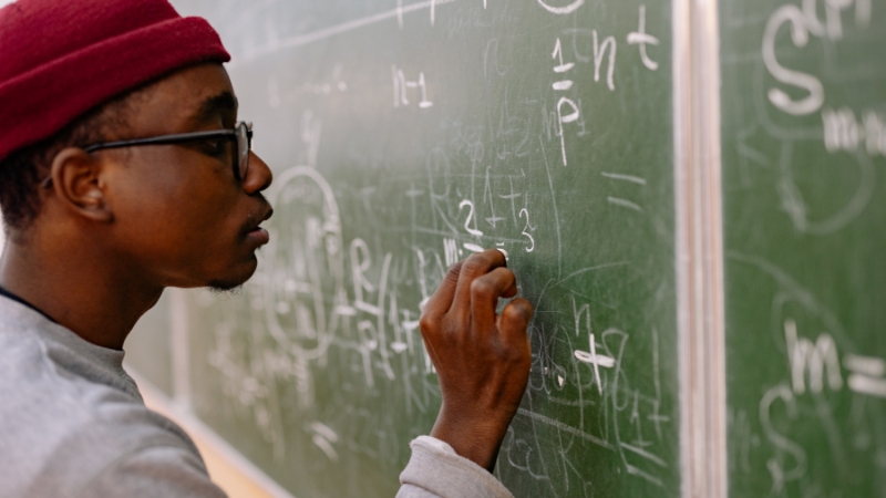 Student writing linear algebra equations on a chalkboard during class